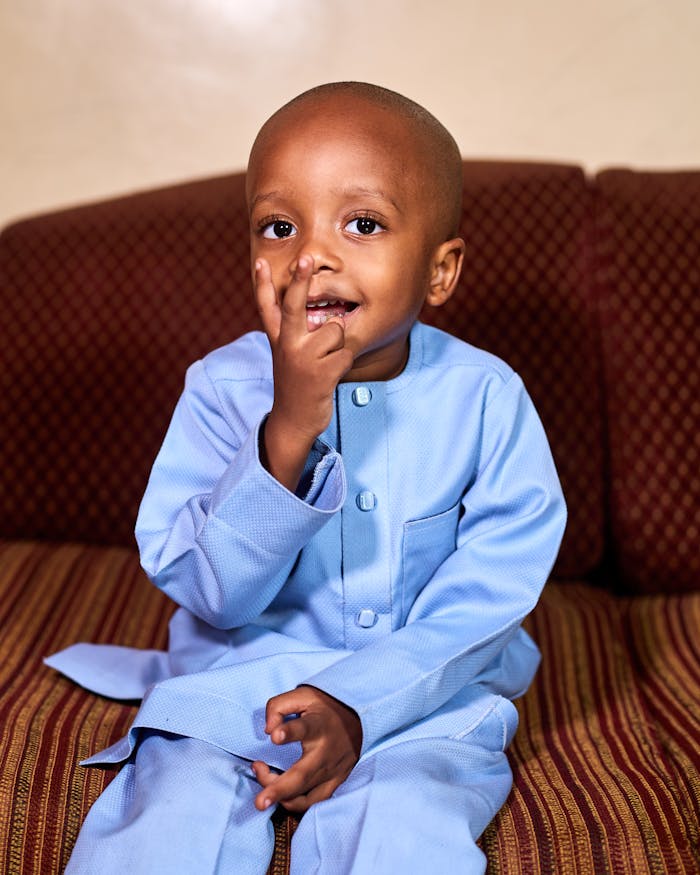 Little boy in a sky‑blue kaftan, chillin' on the sofa with that 'I’m thinkin' big' vibe 😎👑 