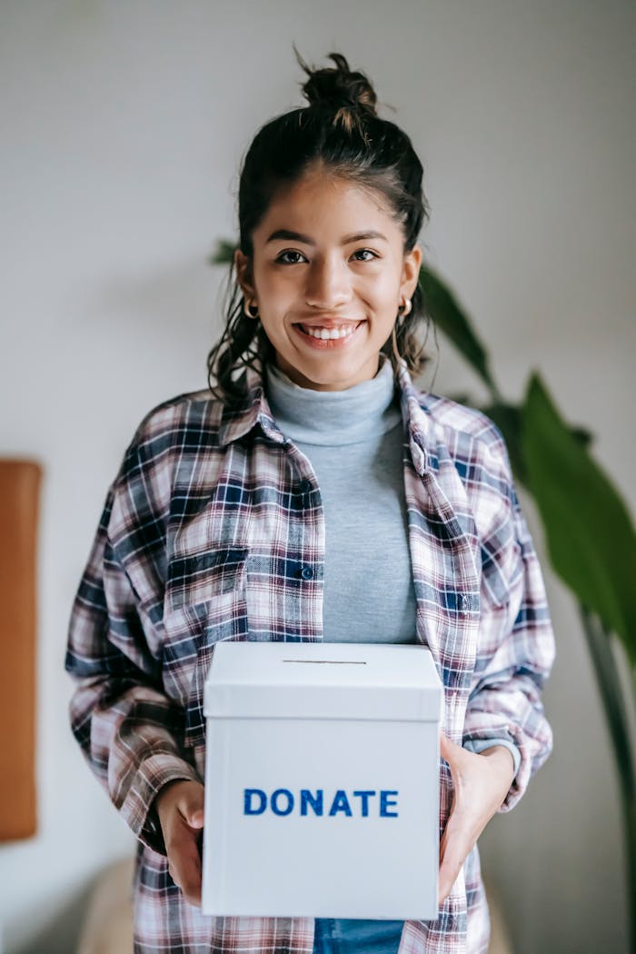 ours-journey Cheerful woman holding a box labeled 'Donate' indoors, symbolizing charity and kindness.